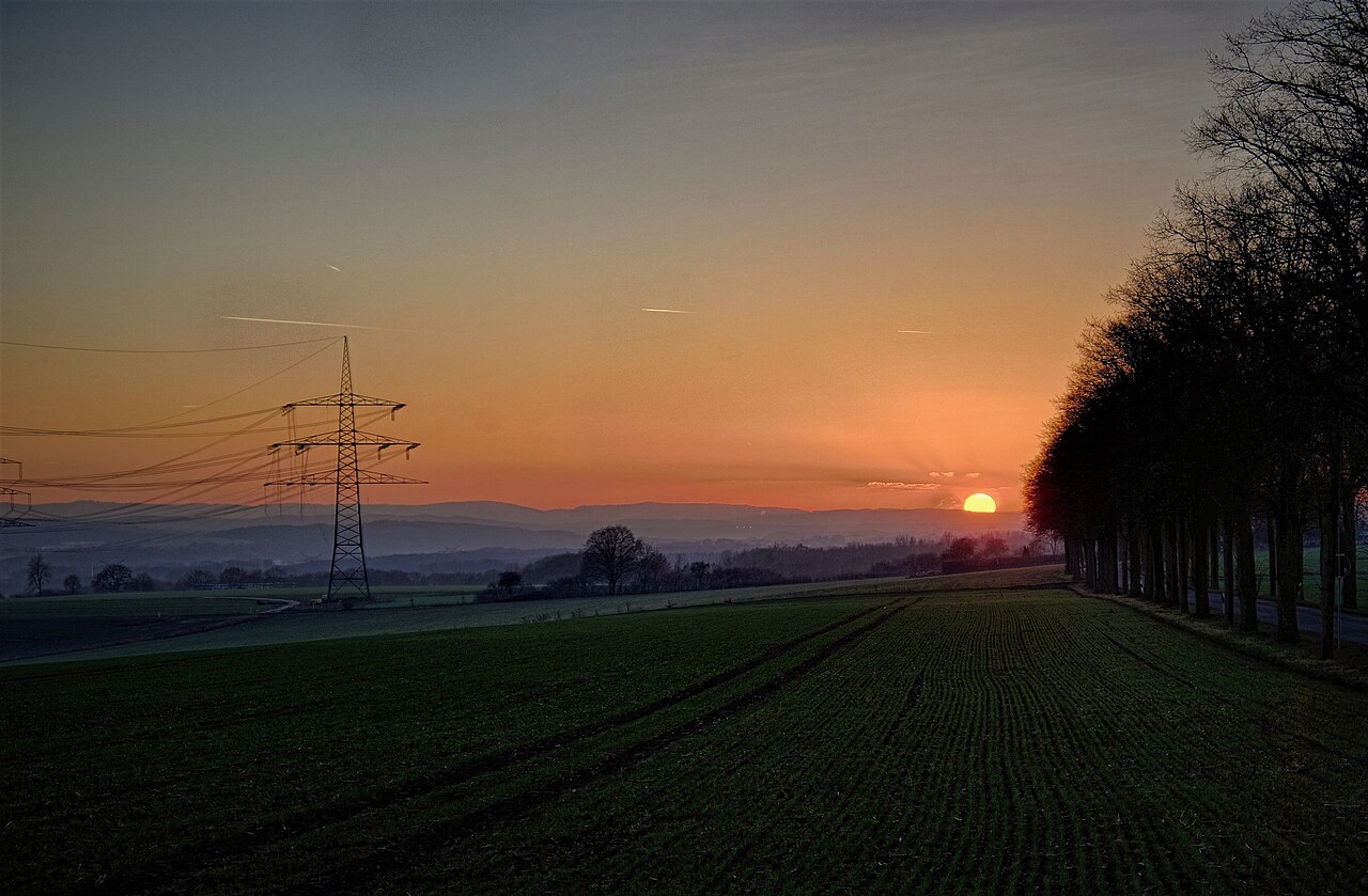 An electricity transmission pylon over a winter crop field at sunset.